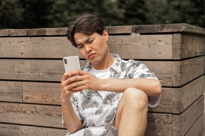 Asian displeased man browsing smartphone in countryside