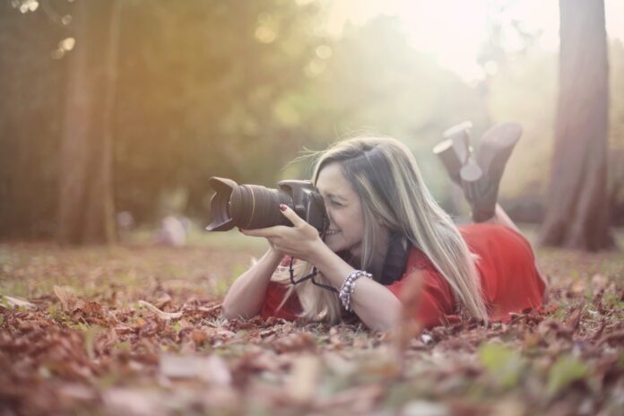 Smiling woman taking photos on professional photo camera in forest