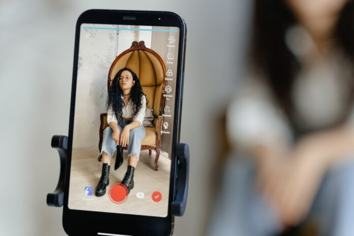 A Close-Up Shot of a Smartphone Recording a Woman Sitting on a Chair