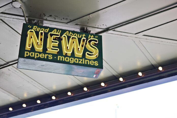 From below of illuminated signboard with news papers magazines inscriptions hanging on metal ceiling on street