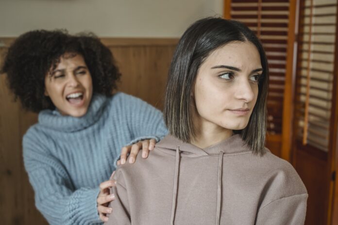 Angry African American female in casual wear screaming and grabbing shoulder of displeased female while having conflict in room at home