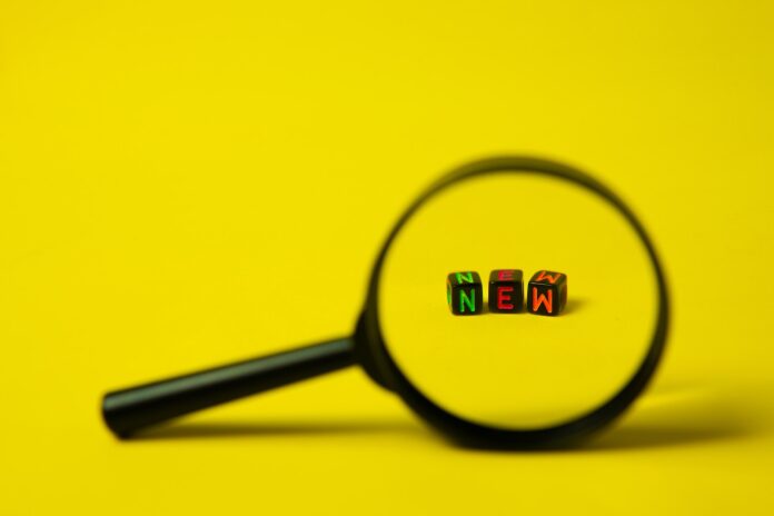 Concept image of big black magnifier with word new in form of cubes against yellow background